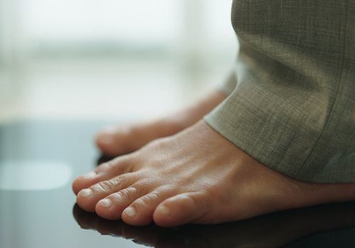 Pés descalços de uma pessoa sobre uma balança digital preta, num ambiente doméstico.