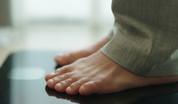 Pés descalços de uma pessoa sobre uma balança digital preta, num ambiente doméstico.